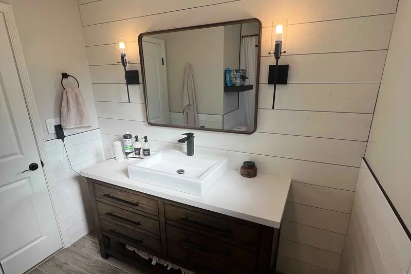 Vanity against a shiplap wall with wall sconces and a black framed mirror