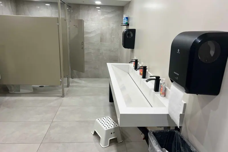 Commercial restroom with a trough sink and floor to ceiling tile