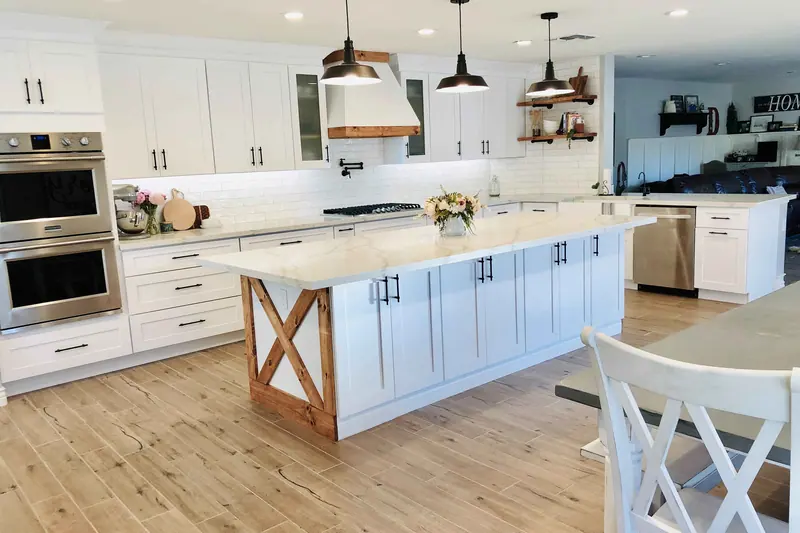 Large white kitchen island lit by black pendant lights in a finished remodel