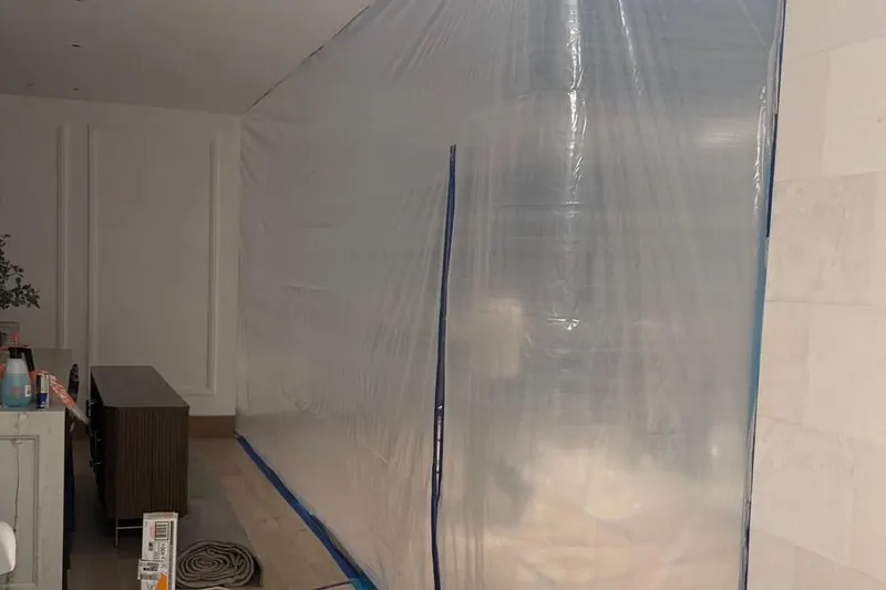 A sealed plastic containment taped from floor to ceiling, with the floor outside it papered and taped